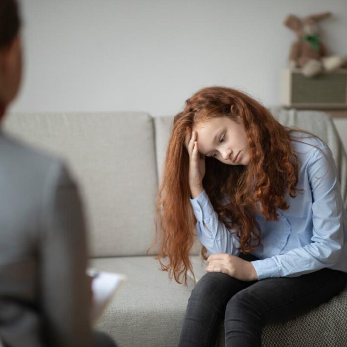 a teen looks sad on a couch talking to a therapist about signs of depression in teens