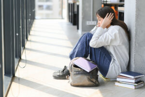 a teen sits on the school floor wondering about signs of prescription drug addiction