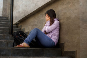 a teen sits on steps with their head in their ahnds to show Adderall addiction signs