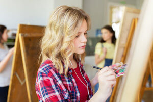 A teen girl paints while considering the benefits of art therapy