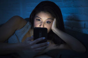 teen girl using cell phone late at night could use cell phone addiction treatment