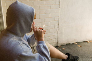 A teen smokes marijuana in an alley to represent the signs of marijuana addiction