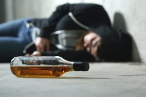 A teen boy lies on the ground next to a liquor bottle as an example of teen alcohol abuse